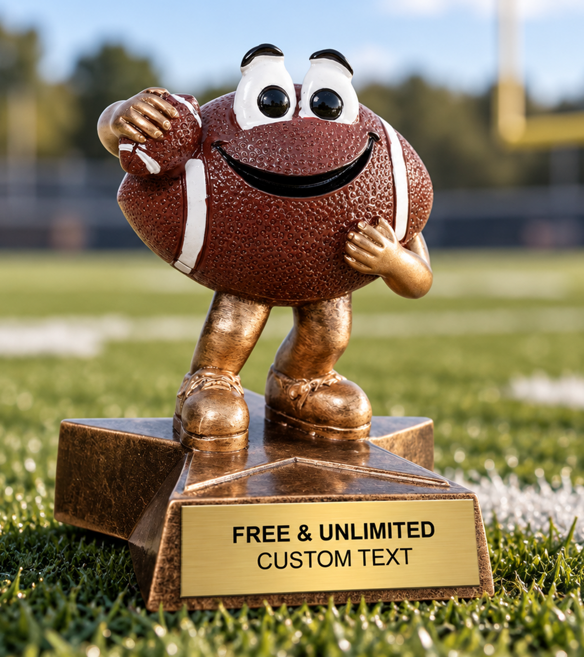A football-shaped cartoon trophy on a bronze base, standing on a grassy field. The football has a textured brown surface with white laces, cartoon eyes, a wide smile, and small legs and shoes.